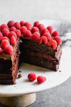 a chocolate cake with raspberries is on a plate and has one slice cut out