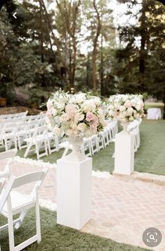 an outdoor ceremony setup with white chairs and flowers in vases on each side of the aisle