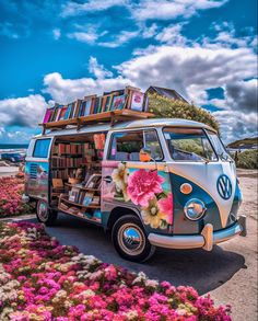 a vw bus with books on the roof parked in front of some flowers and grass