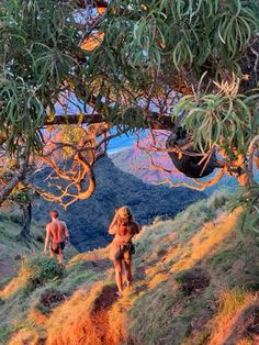 two people walking up a hill with trees on each side and mountains in the background