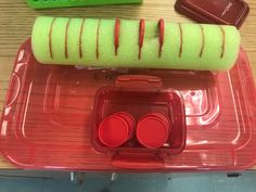 a plastic container filled with red and green items on top of a wooden table next to a remote control