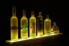 several different types of wine bottles on a shelf with lights in the dark behind them