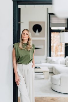 a woman standing in front of a mirror wearing white pants and a green top with her hands on her hips