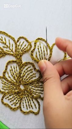 someone is working on a piece of fabric with gold thread and crocheted flowers