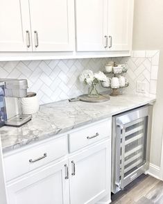 a kitchen with white cabinets and marble counter tops, an ice maker on the left