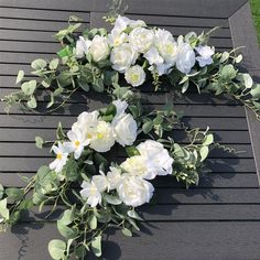 white flowers and greenery are arranged on a black table top with grass in the background