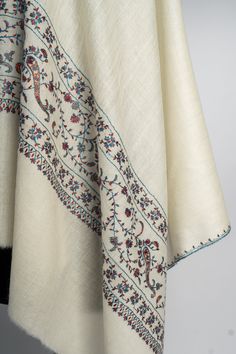 Exude timeless grace with this ivory merino wool scarf, meticulously hand-embroidered with intricate sozni patterns in muted shades. The beautifully crafted vine motifs running across the fabric evoke a sense of elegance, making this scarf a must-have for lovers of understated luxury. Soft to the touch and light to wear, this scarf is perfect for elevating any outfit. Whether for casual outings or formal events, its delicate design and superior craftsmanship ensure it stands out as a true repres Luxury Pashmina Scarves With Resham Embroidery, Luxury Embroidered Elegant Scarf, Embroidered Rug, Scarf Jacket, Embroidered Handbag, Merino Wool Scarf, Silk Carpet, Understated Luxury, Delicate Design