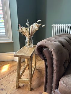 a small wooden table with flowers in a vase on it next to a couch and radiator