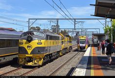 two trains are parked at the train station as people walk on the platform beside them