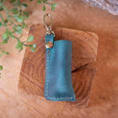 a leather keychain is sitting on top of a piece of wood with a plant in the background