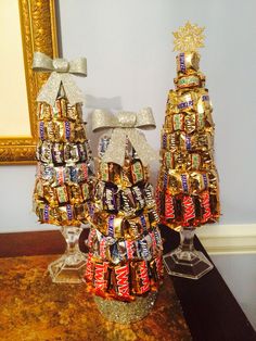 two christmas trees made out of candy bars on a table next to a framed mirror