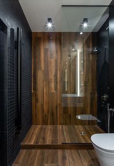 a modern bathroom with wood flooring and black tiles on the walls, along with a glass shower stall