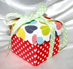 a small red box with polka dots and a green bow on the top is sitting on a white surface