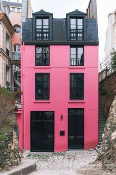 a pink building with black doors and windows on the outside, in front of some buildings