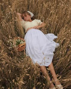 a woman laying in the middle of a field next to a basket with flowers on it