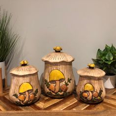 three ceramic jars with designs on them are sitting on a wooden table next to a potted plant