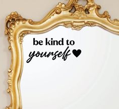 a gold framed mirror with the words be kind to yourself written in black on it