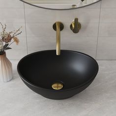 a black bowl sink sitting on top of a counter next to a vase with flowers