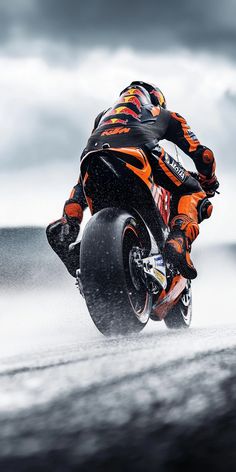 a man riding on the back of a motorcycle down a wet road in front of dark clouds