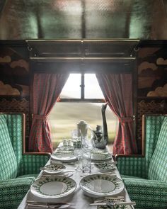 a long table with plates and silverware on it in front of a window that has red curtains