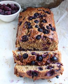 a loaf of blueberry bread sitting on top of a counter next to a bowl of berries