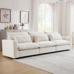 a living room filled with white furniture and large window covered in curtains on the windowsill