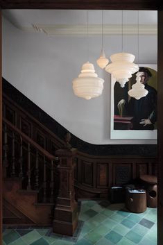 a painting hangs on the wall next to a stair case with two lamps hanging from it