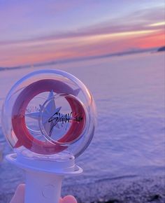 someone is holding up a plastic object near the water at sunset or sunrise, and it looks like they are spinning around