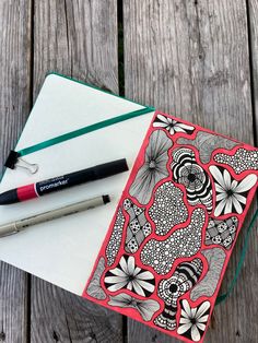 an open notebook sitting on top of a wooden table next to a pen and marker