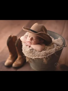 a baby wearing a cowboy hat sleeping in a bucket with his hands under his chin