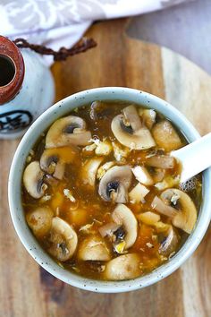 a bowl of soup with mushrooms in it on a wooden table next to a cup of coffee