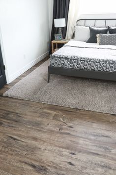 a bed sitting on top of a wooden floor next to a white wall and window