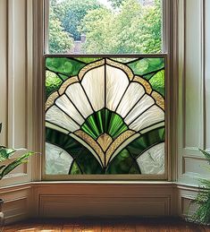 a stained glass window with green leaves in the center and white trim around it, sitting on a wooden floor