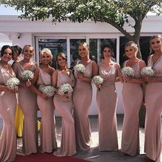 a group of women standing next to each other in front of a white building holding bouquets