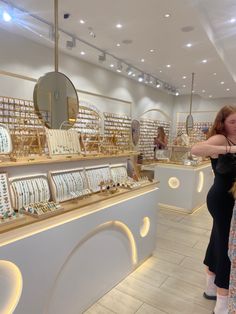 two women looking at jewelry on display in a store with white walls and flooring