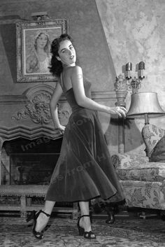 an old photo of a woman standing in front of a fire place wearing a dress