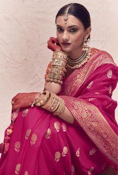 a woman in a pink sari sitting down with her hand on her chin and wearing gold jewelry