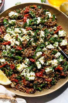 a plate filled with lentils, feta cheese and lemon wedges on top