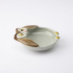 an owl shaped bowl with yellow eyes on the bottom and one eye open, sitting in front of a white background