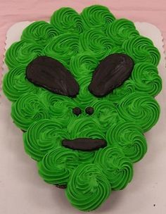 a green monster cake with black icing on it's face and eyes, sitting on top of a white plate