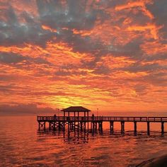 the sun is setting over an ocean with a pier in the foreground