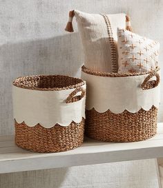 two woven baskets sitting on top of a wooden shelf next to a pillow and throw pillow