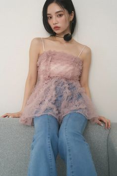 a young woman sitting on top of a couch wearing blue jeans and a pink top