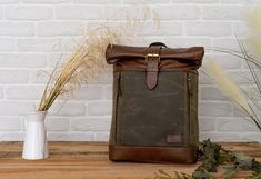 a brown leather backpack sitting on top of a wooden table next to a white vase