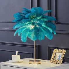 a blue palm tree in a gold vase next to a white table with a cup and saucer on it