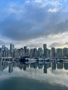 boats are docked in the harbor with tall buildings in the background and clouds in the sky