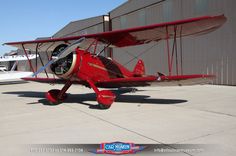 a small red airplane sitting on top of an airport tarmac next to a building