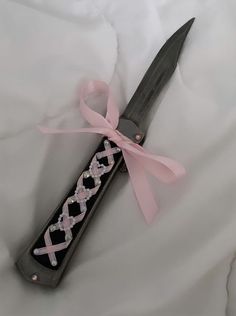 a pink ribbon tied around a knife on top of a white sheet with black handles