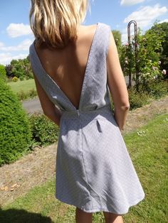 the back of a woman's dress is seen in this image, with grass and bushes behind her