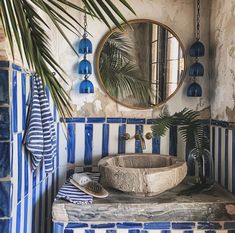 a bathroom with blue and white tiles on the walls, a round mirror hanging above the sink